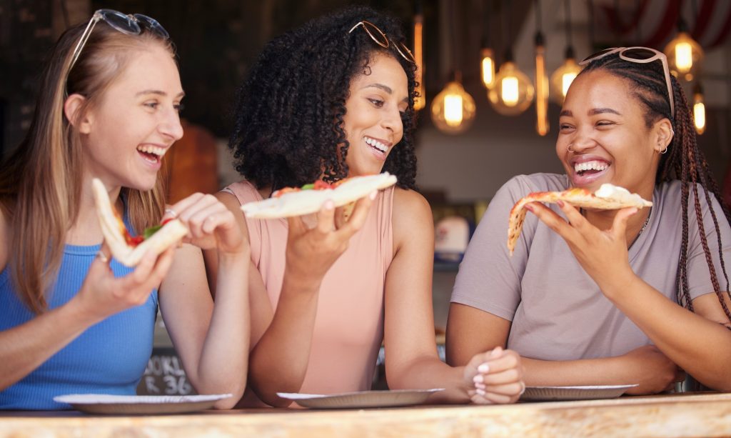Woman, friends and laughing for pizza, food or eating at funny restaurant together in friendship. H